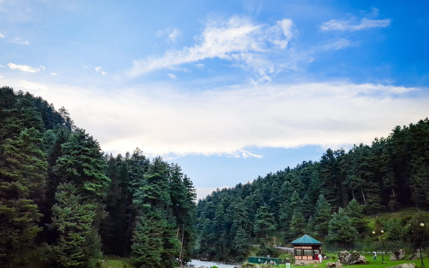 A winding river through a green mountain meadow under a soft blue sky